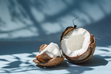 Half a coconut and pieces of coconut on a blue background. - obrazy, fototapety, plakaty