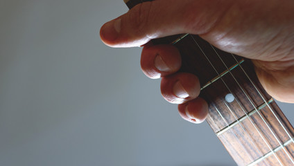 Hand holding the neck and fretboard of an electric guitar against a grey background