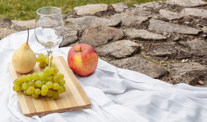Picnic in the nature in the park. A glass of wine green grapes yellow pear red apple lilac on a...