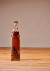 Transparent bottle of homemade chilli oil with pieces of dry chilli, on a wooden table