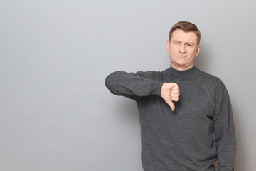 Portrait of dissatisfied man showing thumb down in disapproval gesture