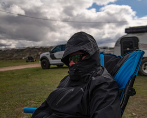 A man on a windy day with a rain jacket and sunglasses on.