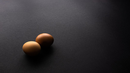Two organic eggs on black texture background, office desk table from top view, copy space. 