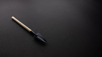 Light brown wood stick with black steel shovel on black texture background, office desk table from...