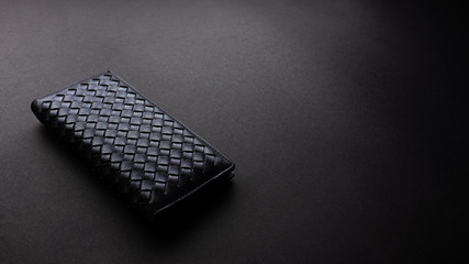 Black leather long wallet on black texture background, office desk table from top view, copy space. 