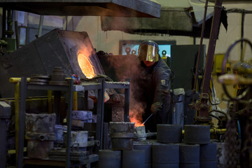 Worker man pours molten metal into molds at a steel mill