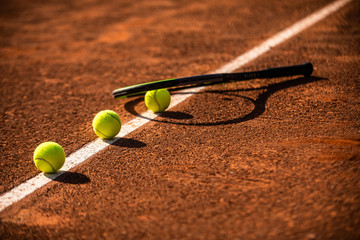 raquette au sol avec trois de tennis sur une ligne blanche de terre battue