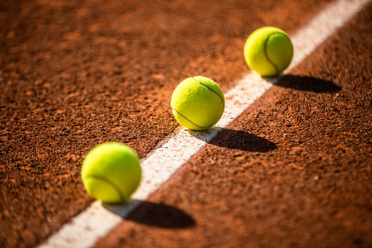trois balles de tennis sur une ligne blanche de terre battue