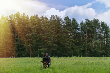Fototapeta premium A man works at a table with a laptop in an empty field. Remote work in the field
