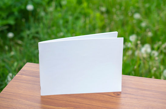 Clean and blank landscape magazine catalog on the wooden table with blurred green grass background behind as template for your design presentation, print promotion, portfolio etc.