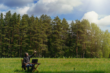 Fototapeta na wymiar A man works at a table with a laptop in an empty field. Remote work in the field