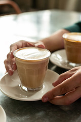 Vertical frame, side view - men's hands on both sides holding a transparent glass full of coffee, standing on the bar counter. Concept of increasing brain activity