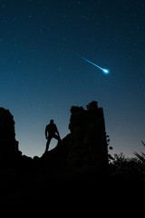 Man standing on ruins on starry sky with falling star