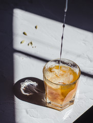 Iced black tea with coconut milk, honey and cardamon. Refreshing and aromatic drink. Pouring milk to the glass with iced tea. Background. Copy space.