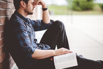 Lonely depressed person sitting near a brick wall with the Bible on his lap