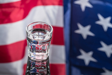 Vodka in shot glass on mirror background with American flag reflected in it. Independence Day Drink