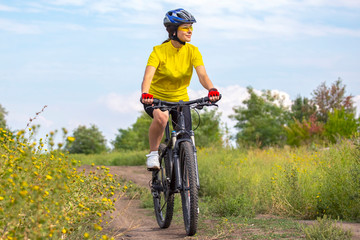 Beautiful girl in yellow riding a bike in nature. Sports and recreation. Hobbies and health.