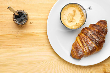 Top view on a breakfast consisting of a cup of coffee, a croissant with jam on a wooden table with copy space