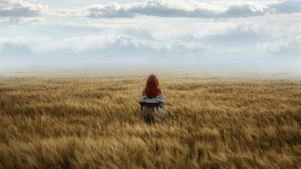 Red-haired girl sits at sunset in a wheat field. Silhouette.