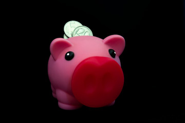 Pink piggy bank full of coins on a black background. Concept of where to invest your savings. Make money