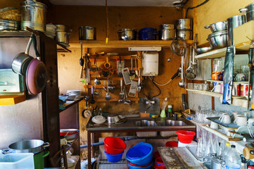 Wide angle view on the kitchen rustic old natural with a lot of dishes plates and utensil sink and boiler in cabin full stacked in the village on farm
