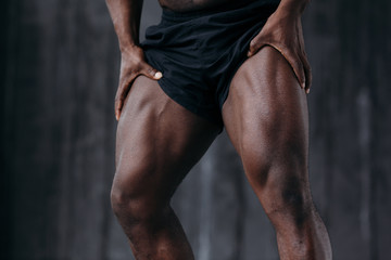 Close-up front muscles of the upper thigh of a black professional athlete in black shorts.