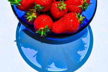 Delicious red ripe strawberries in a blue vase on the white background. Beautiful art shadows of berries in a bowl.