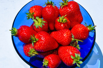 Delicious red ripe strawberries in a blue vase on the white background. Beautiful art shadows of berries in a bowl.