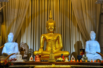 Golden Buddha statue with two white Buddhist statues on both sides on the beige curtain background. Buddhism concept.