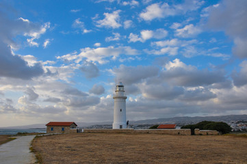 Solitary, white, beautiful lighthouse standing in the wild field under the scenic cloudy sky.