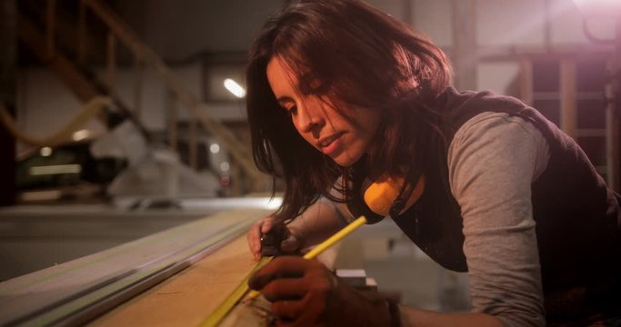 Woman measuring wooden board in a carpentry workshop