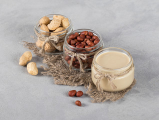Peanut paste, peeled peanuts, peanuts in husks in jars in rustic style on a light background copy space