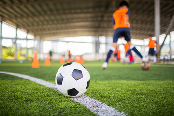 Football on green artificial turf with blurry soccer team training.