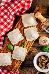 Homemade fresh Italian ravioli pasta with mushrooms on rustic wooden background.