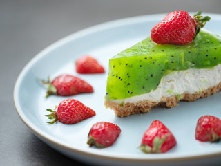 close up view to kiwi cake with red strawberries on blue plate
