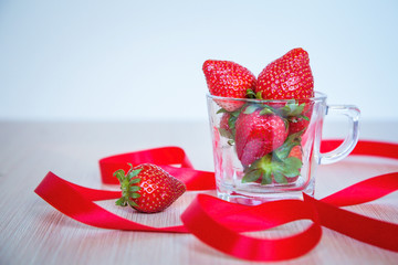 fresh, ripe, red strawberries in a transparent Cup, with a red ribbon, on a light background