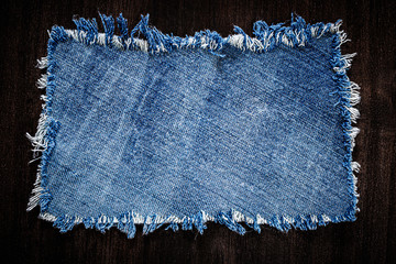 Denim blue cloth frame patch on wooden table. Denim jeans frame background. Ripped denim fabric,...
