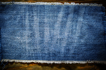Denim blue cloth frame patch on wooden table. Denim jeans frame background. Ripped denim fabric,...