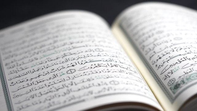 Dramatic Closeup of light illuminating The Muslim Quran, religious book  on a table in the dark while it passes over it