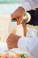 A man in a white shirt pours champagne into a glass, hands closeup.