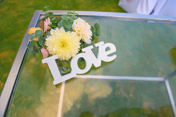 The word Love made of wood with flowers lies on a glass table.