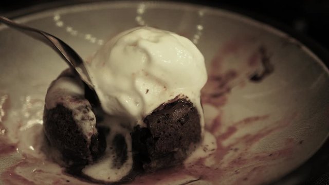 Dessert fondant, ice cream ball on hot chocolate cake on plate, breaks a chocolate cake, liquid chocolate flows, child tongue lick dessert, toned, close up