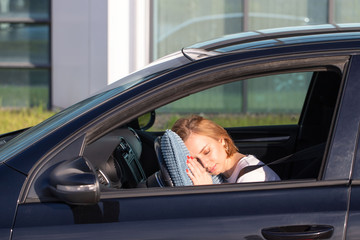 Fototapeta na wymiar Tired young woman driver asleep on pillow on steering wheel, resting after long hours driving a car. Fatigue. Sleep deprivation. 