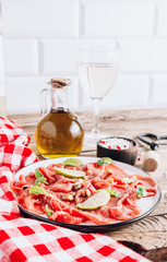 White plate with carpaccio of beef with baby arugula, lime and white wine on rustic wooden...