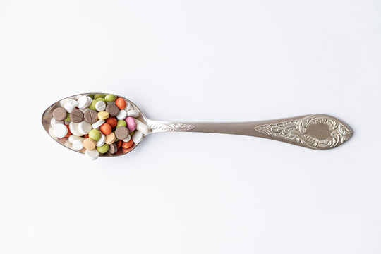 Medicine and health, treatment, pharmaceutics, coronavirus, pandemic, epidemic concept - layout one silver big tablespoon with multi-colored tablets and capsules on a white background copy space.