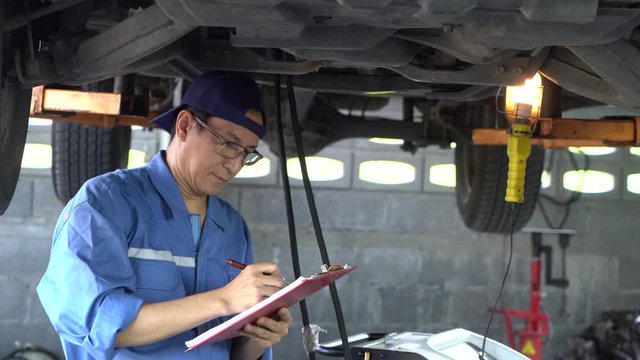Asian Man mechanic inspection writing note on clipboard insurance notepad with car engine.for transport automobile automotive image.
