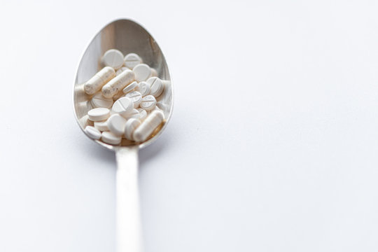 Medicine and health, treatment, pharmacy, coronavirus, pandemic, epidemic concept - layout one silver big tablespoon with different pills and capsules on a white background copy space.
