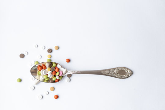 Medicine and health, treatment, pharmaceutics, coronavirus, pandemic, epidemic concept - layout one silver big tablespoon with multi-colored tablets and capsules on a white background copy space.