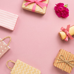 Gift boxes and shopping bags with carnation flower on pink background. Anniversary concept, flat lay, top view, copy space