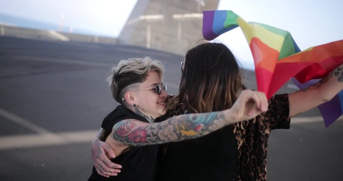 Lesbian couple embracing each other holding LGBT pride rainbow flag